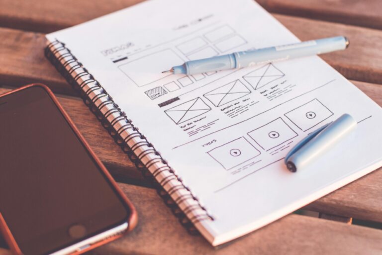 One Page Close-up of a notebook with wireframe sketches and a smartphone on a wooden desk.