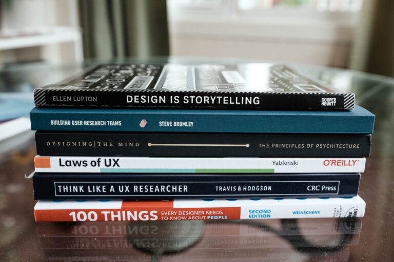One Page A close-up of books focused on design and UX research stacked on a glass table.